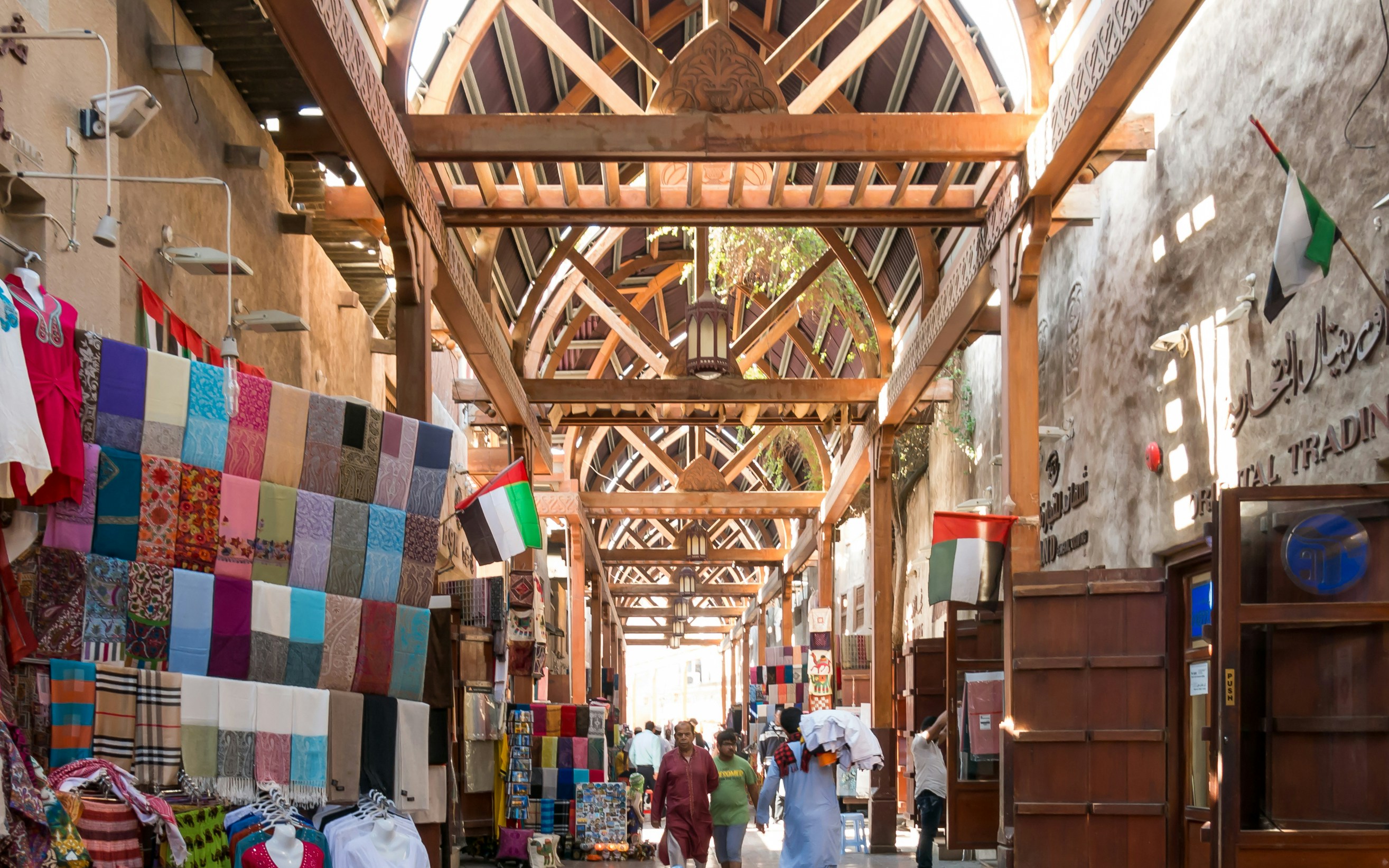 Dubai market with textiles and flags under wooden arches, part of Old & New Dubai Tour.