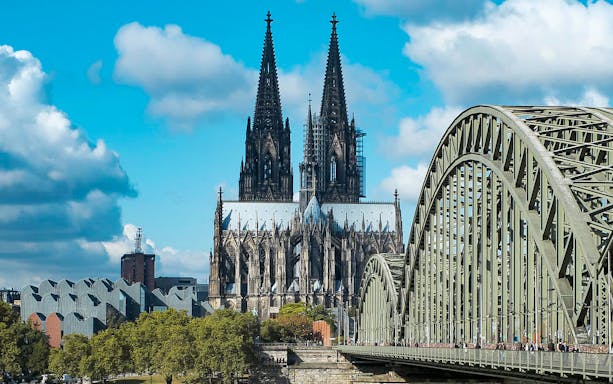 Cologne Cathedral exterior with Hohenzollern Bridge in foreground.