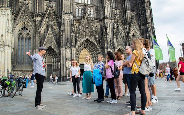 Tour group listening to a guide in front of Cologne Cathedral, Germany.