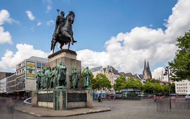 Equestrian statue in Cologne square with cathedral spires in the background.
