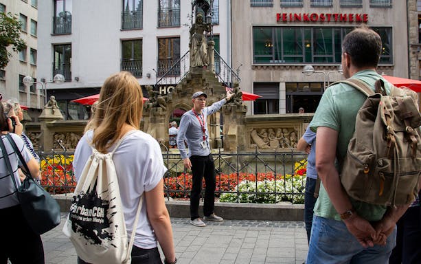 Tour guide explaining a historic fountain to a group in Cologne's city center.