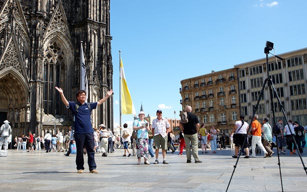 Tourists in front of Cologne Cathedral, Germany, with a camera on a tripod.
