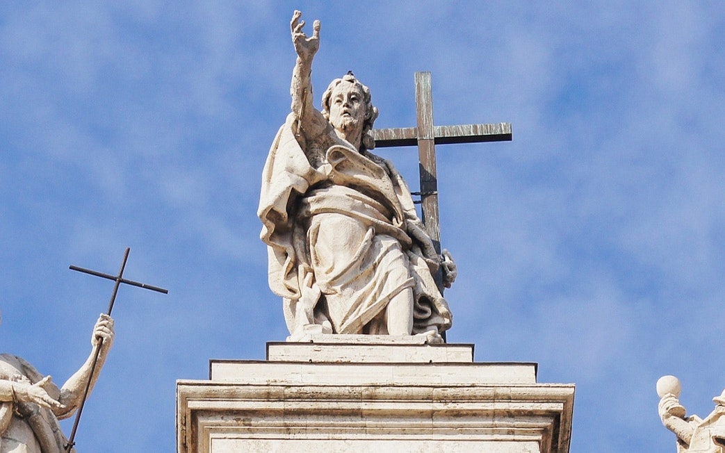 Statue atop St. John Lateran Basilica in Rome holding a cross.