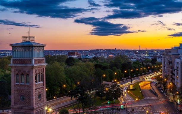 Sunset view of Madrid skyline with historic tower and city lights.