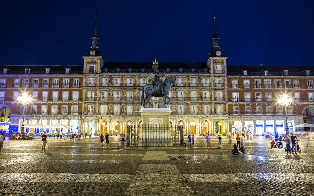 Plaza Mayor in Madrid at night with equestrian statue and illuminated buildings.