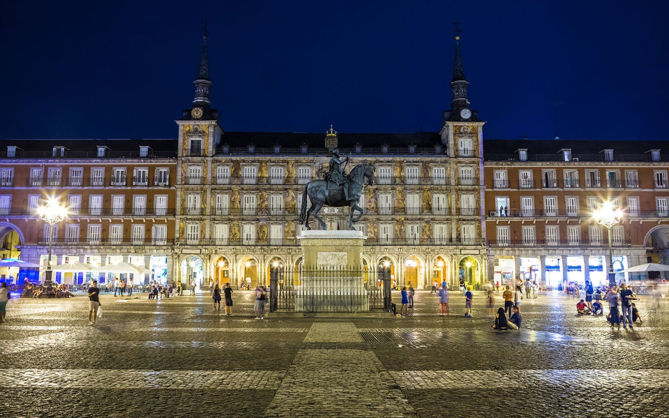 Plaza Mayor in Madrid at night with equestrian statue and illuminated buildings.