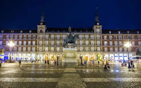 Plaza Mayor in Madrid at night with equestrian statue and illuminated buildings.