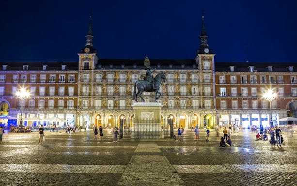 Plaza Mayor in Madrid at night with equestrian statue and illuminated buildings.