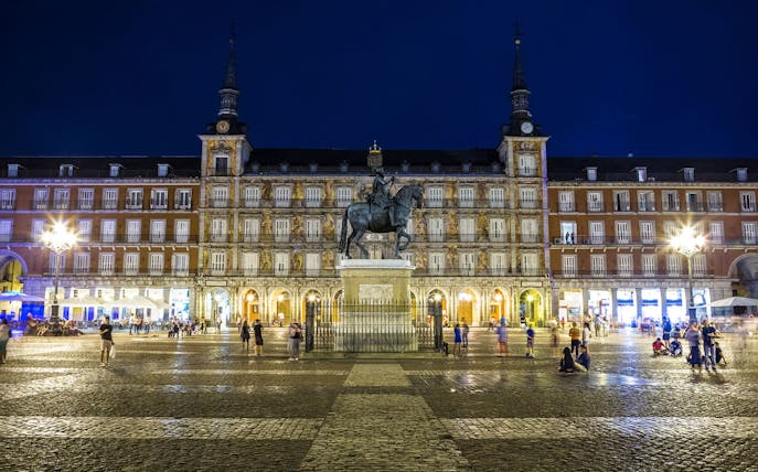 Plaza Mayor in Madrid at night with equestrian statue and illuminated buildings.