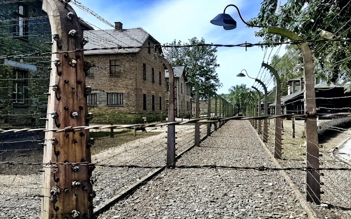 Barbed wire fence and brick buildings at Auschwitz-Birkenau, Poland.