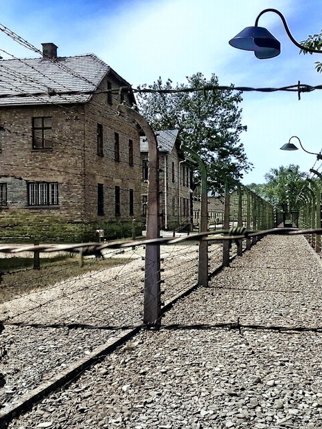 Barbed wire fence and brick buildings at Auschwitz-Birkenau, Poland.