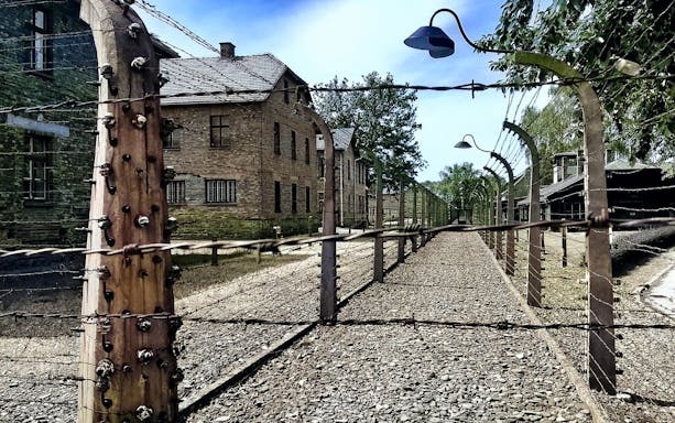 Barbed wire fence and brick buildings at Auschwitz-Birkenau, Poland.