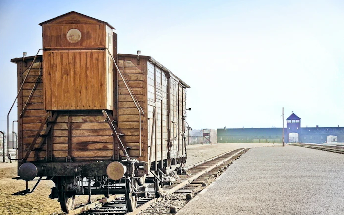 Wooden train car on tracks at Auschwitz-Birkenau, with entrance gate in the distance.