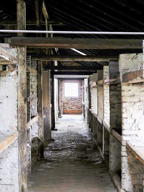 Auschwitz-Birkenau barracks interior with wooden bunks, part of Warsaw tour.