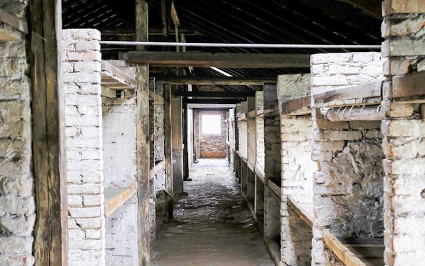 Auschwitz-Birkenau barracks interior with wooden bunks, part of Warsaw tour.