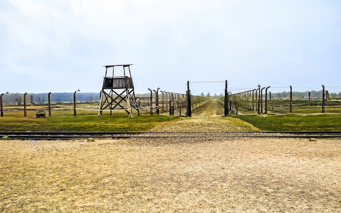 Auschwitz-Birkenau entrance with barbed wire fences and watchtower, part of Warsaw tour.
