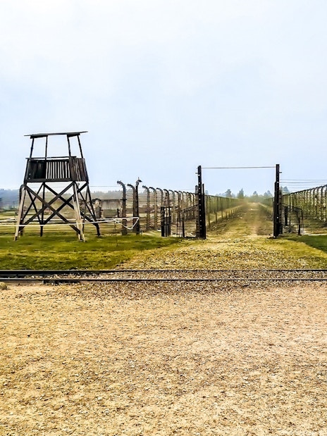 Auschwitz-Birkenau entrance with barbed wire fences and watchtower, part of Warsaw tour.