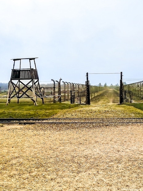Auschwitz-Birkenau entrance with barbed wire fences and watchtower, part of Warsaw tour.