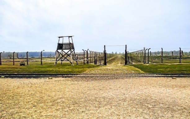 Auschwitz-Birkenau entrance with barbed wire fences and watchtower, part of Warsaw tour.