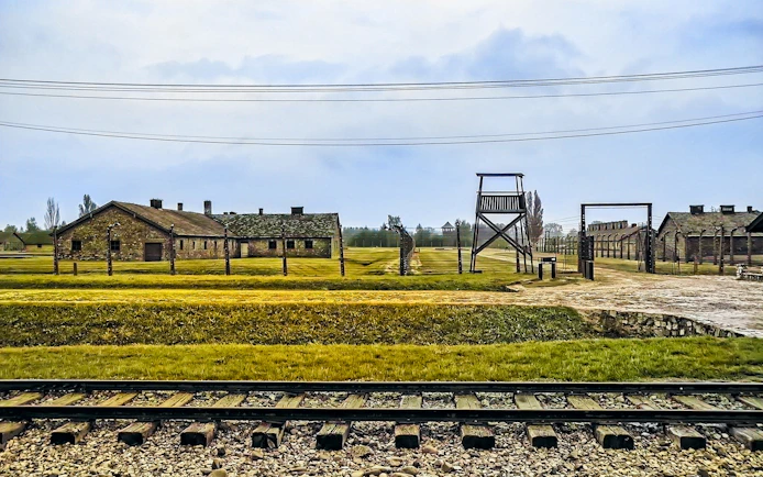 Auschwitz-Birkenau camp buildings and watchtower with railway tracks in foreground.