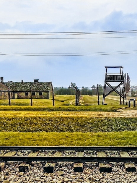 Auschwitz-Birkenau camp buildings and watchtower with railway tracks in foreground.
