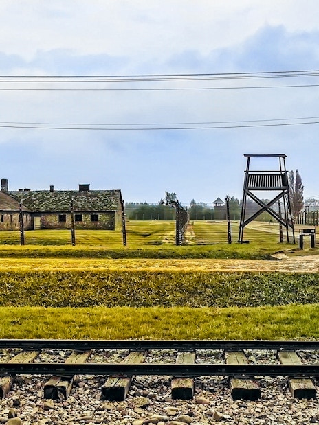 Auschwitz-Birkenau camp buildings and watchtower with railway tracks in foreground.
