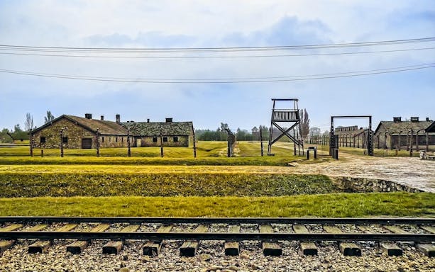 Auschwitz-Birkenau camp buildings and watchtower with railway tracks in foreground.