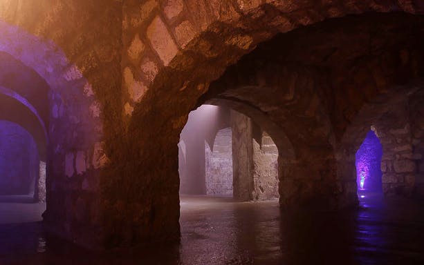 Buda Castle Cave stone arches with ambient lighting on English guided tour.