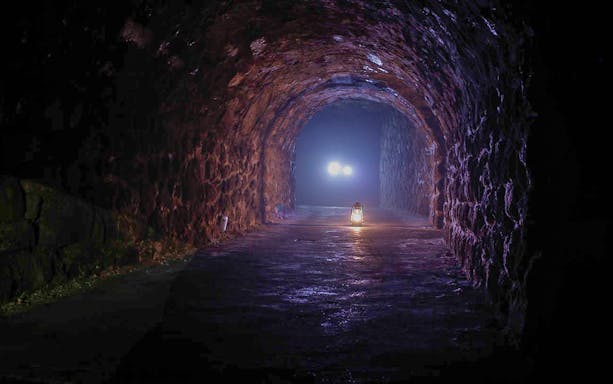 Lantern-lit stone tunnel in Buda Castle Cave during English guided tour.