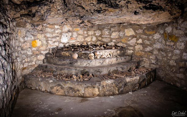 Skulls and bones displayed on stone steps inside Buda Castle Cave during English guided tour.
