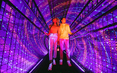 Visitors exploring a vibrant light tunnel at Illuseum Berlin.