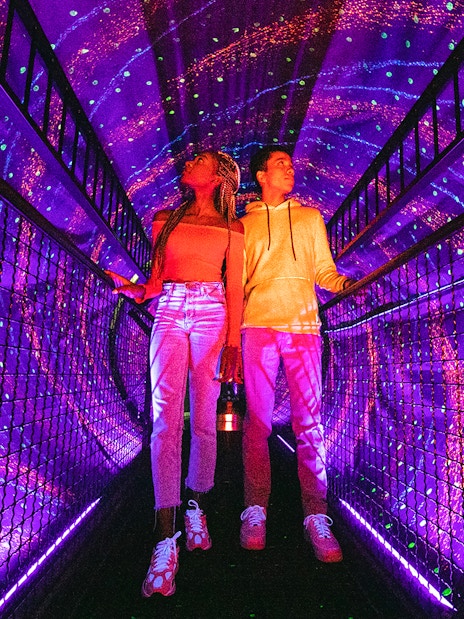 Visitors exploring a vibrant light tunnel at Illuseum Berlin.