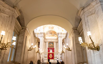 Grand staircase inside Royal Palace of Madrid with ornate chandeliers and royal emblems.