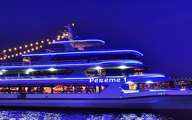 Bosphorus dinner cruise ship illuminated at night with city lights in the background.