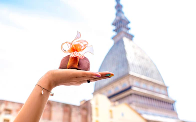 Hand holding a chocolate dessert with Mole Antonelliana in Turin, Italy in the background.
