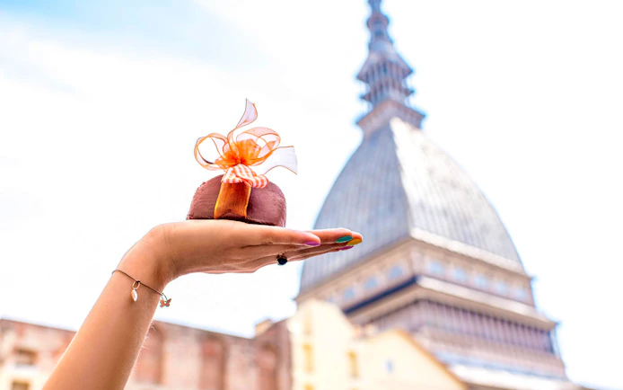 Hand holding a chocolate dessert with Mole Antonelliana in Turin, Italy in the background.