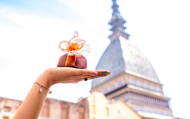 Hand holding a chocolate dessert with Mole Antonelliana in Turin, Italy in the background.