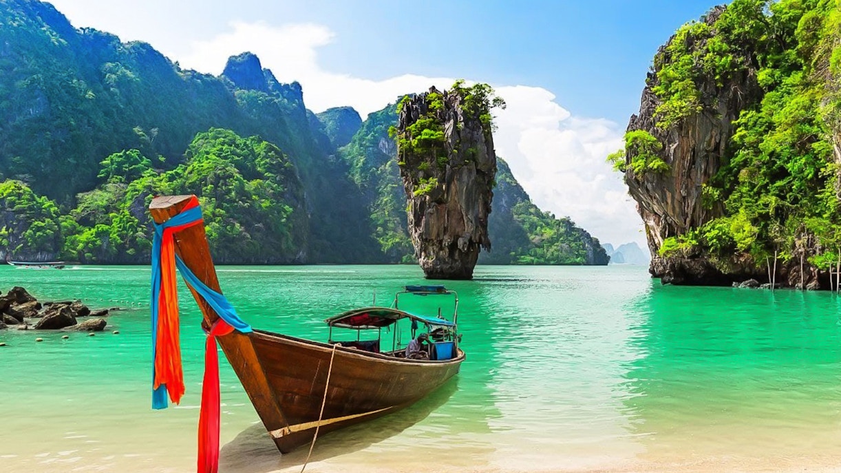 Longtail boat on the shore with James Bond Island in the background, Phang Nga Bay, Thailand.