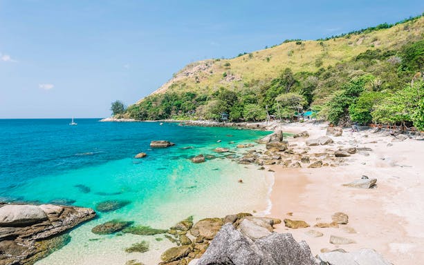 Secluded beach with turquoise waters and rocky shoreline in Phuket, Thailand.