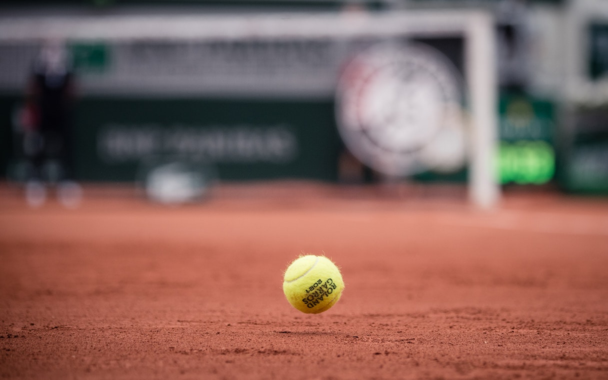 Tennis ball on clay court at Roland Garros Stadium.