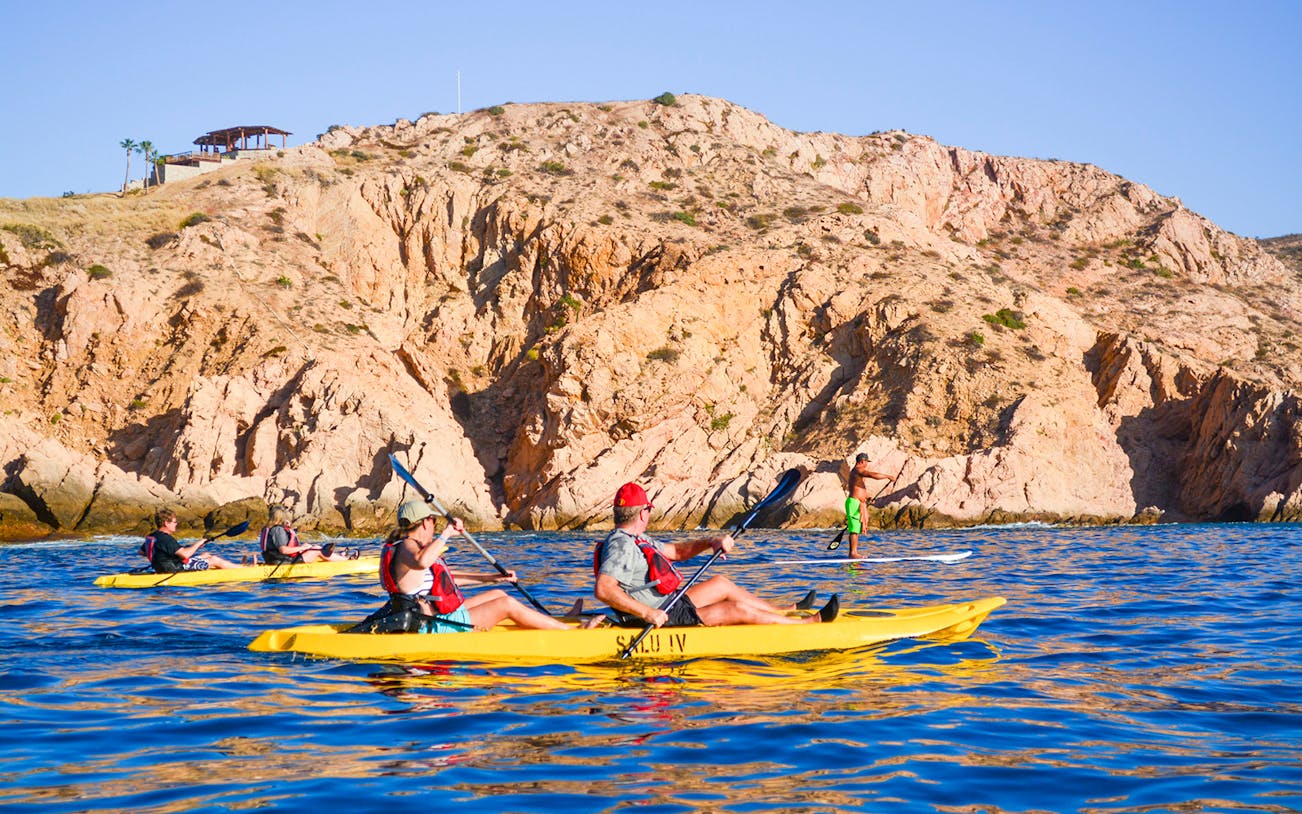 Kayakers paddling near rocky cliffs in Cabo on a private glass bottom kayak tour.