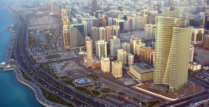 Aerial view of Abu Dhabi skyline with modern skyscrapers and coastal road.