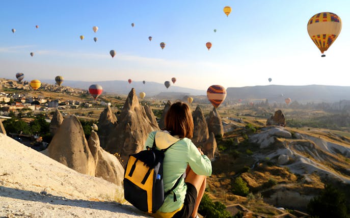 Person overlooking hot air balloons over Cappadocia's unique rock formations.