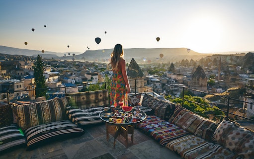 Woman enjoying hot air balloons over Cappadocia from a terrace in Turkey.