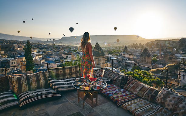 Woman enjoying hot air balloons over Cappadocia from a terrace in Turkey.