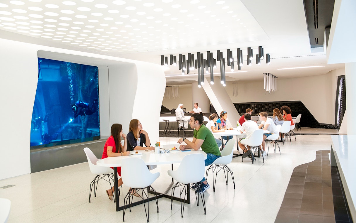 Divers exploring underwater at Deep Dive Dubai, viewed from a modern dining area.