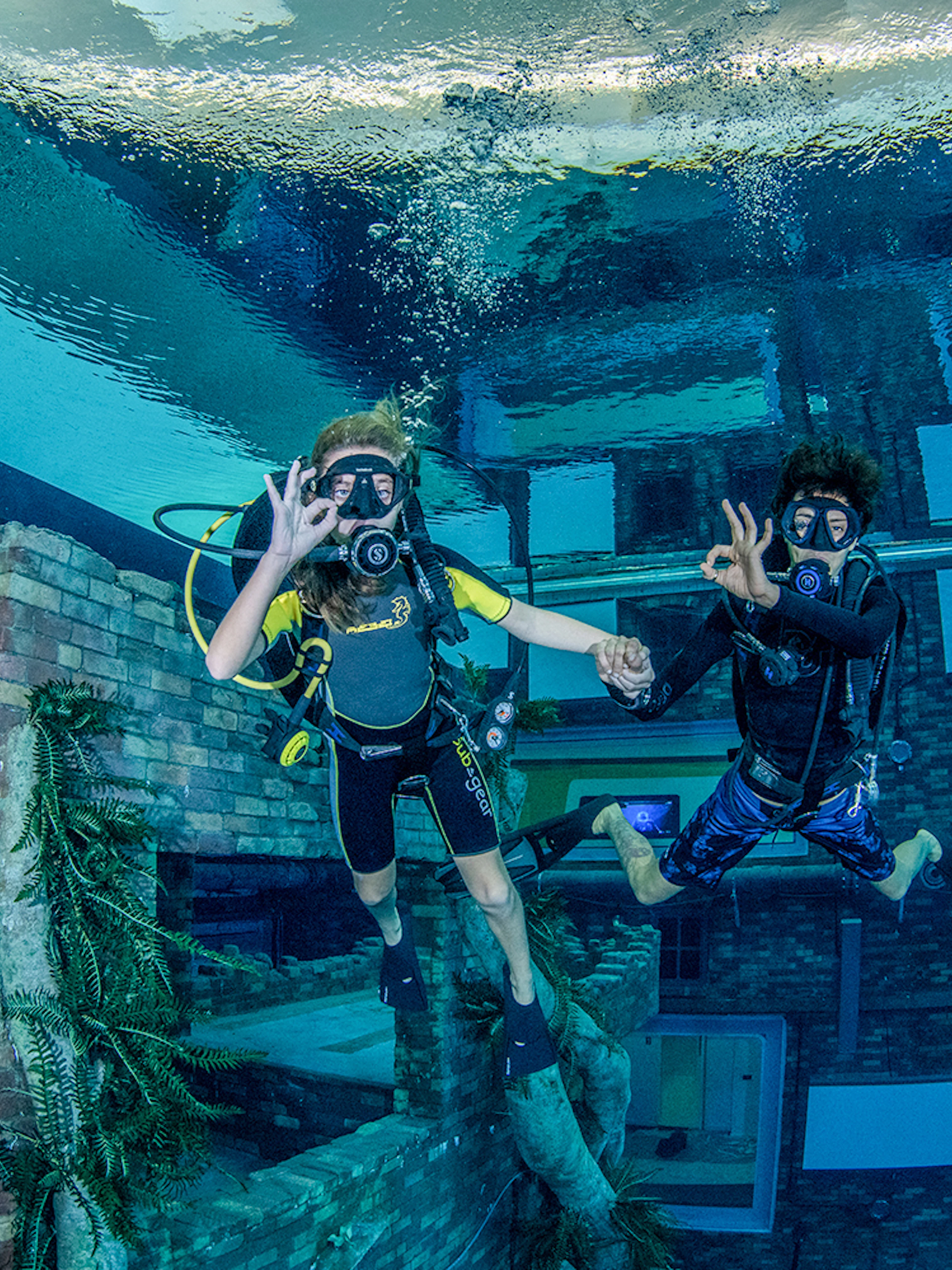 Scuba divers exploring underwater cityscape at Deep Dive Dubai.
