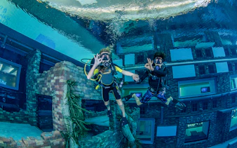 Scuba divers exploring underwater cityscape at Deep Dive Dubai.
