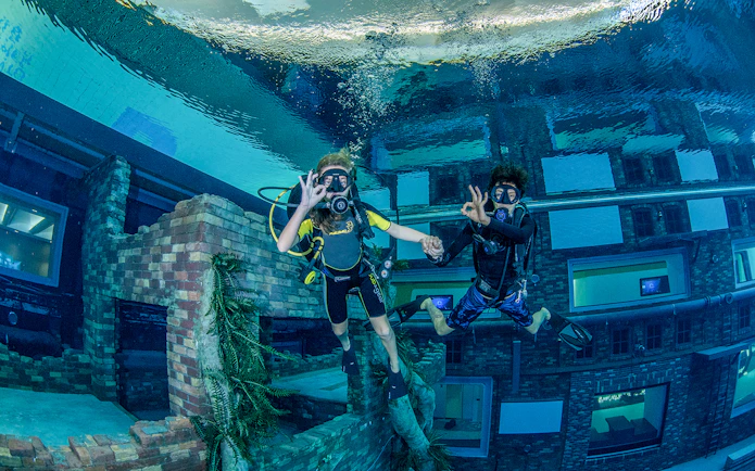 Scuba divers exploring underwater cityscape at Deep Dive Dubai.