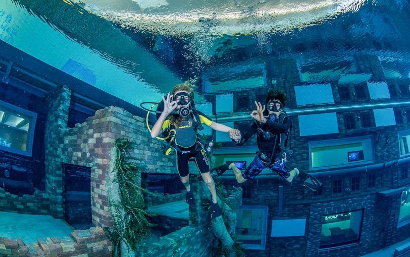Scuba divers exploring underwater cityscape at Deep Dive Dubai.